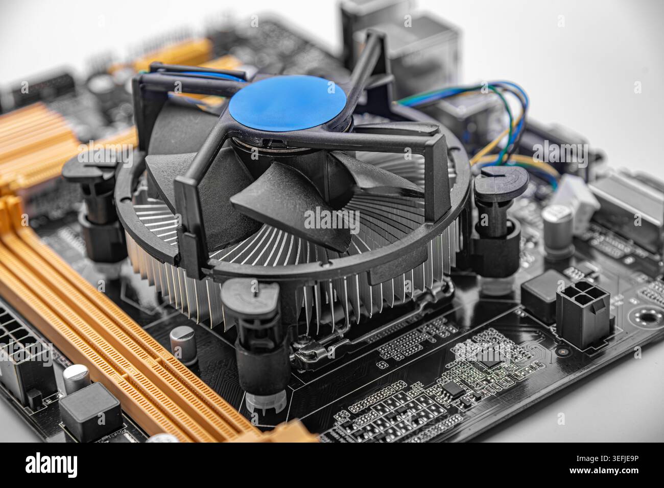 CPU cooler mounted on a black and orange computer motherboard. Stock Photo