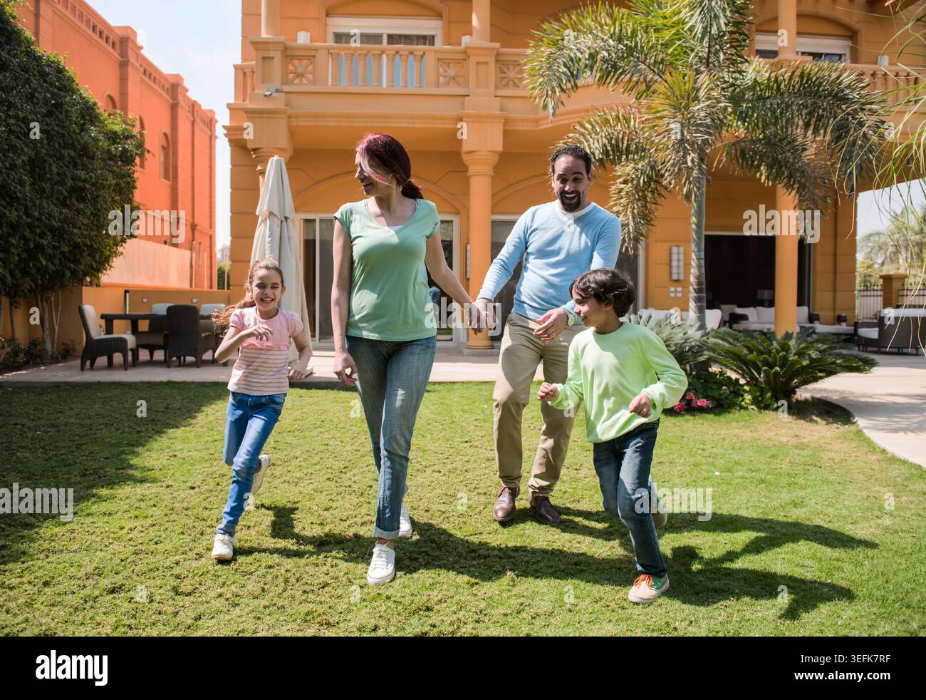 Happy family walking and playing together in a sunny villa garden holding hands Stock Photo