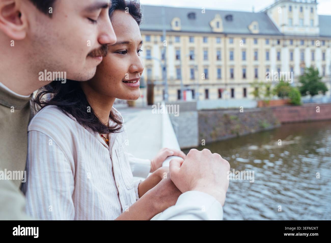 Young diverse couple standing near glass building facade in European city Stock Photo