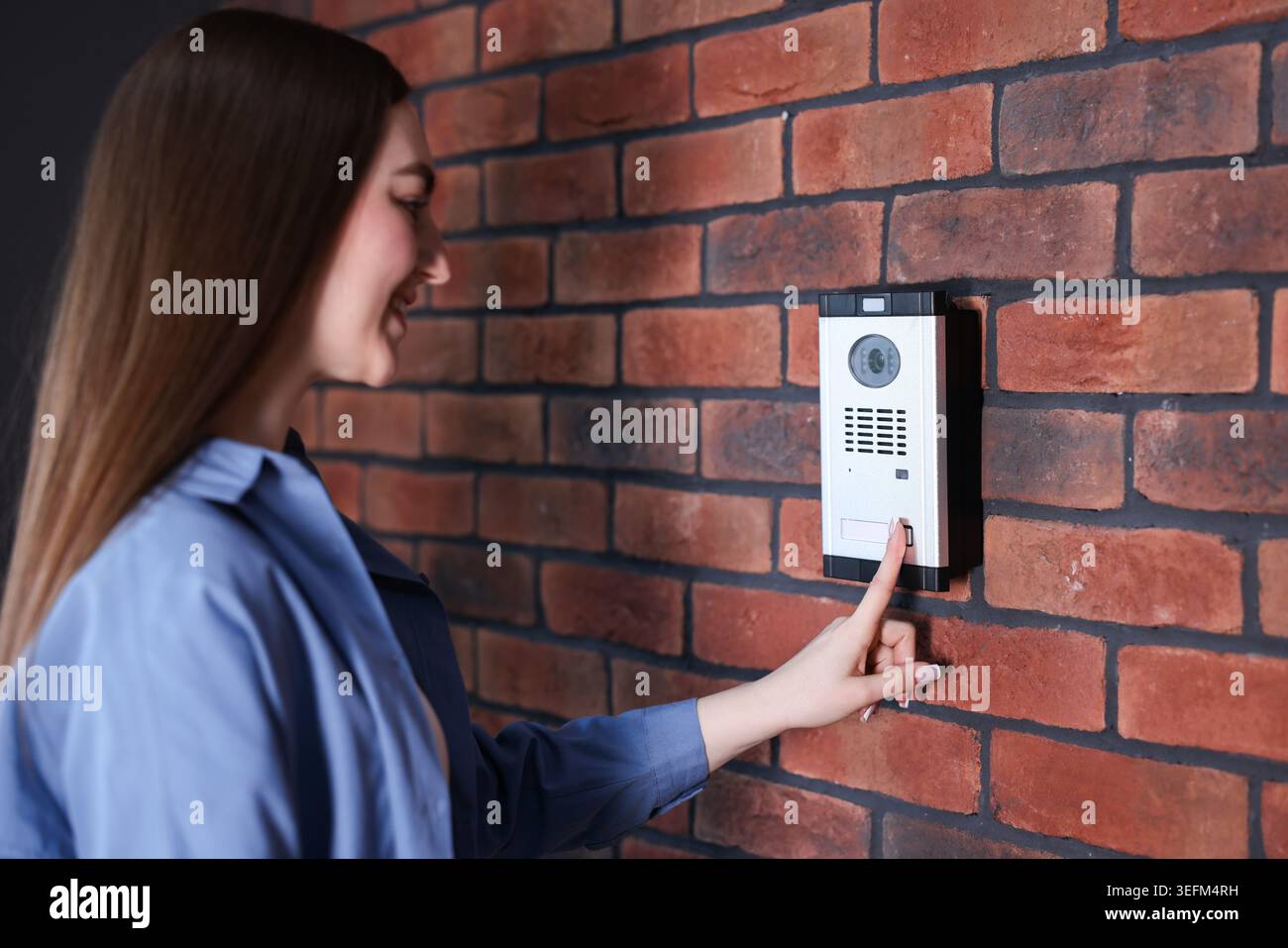 Woman pressing button on intercom panel near brick wall Stock Photo