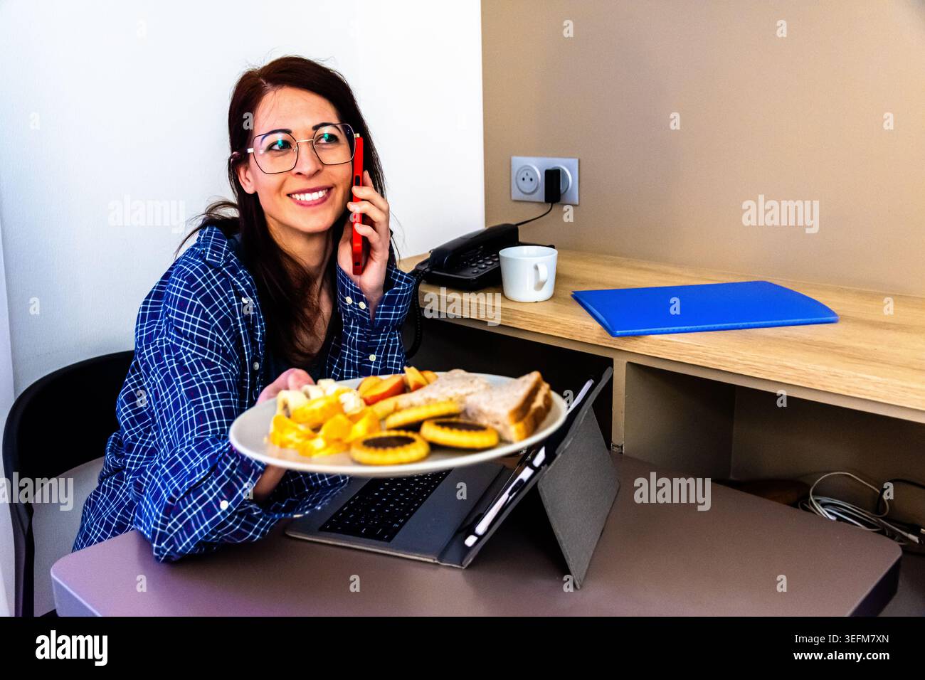 Woman multitasking working remotely having breakfast and talking on phone Stock Photo