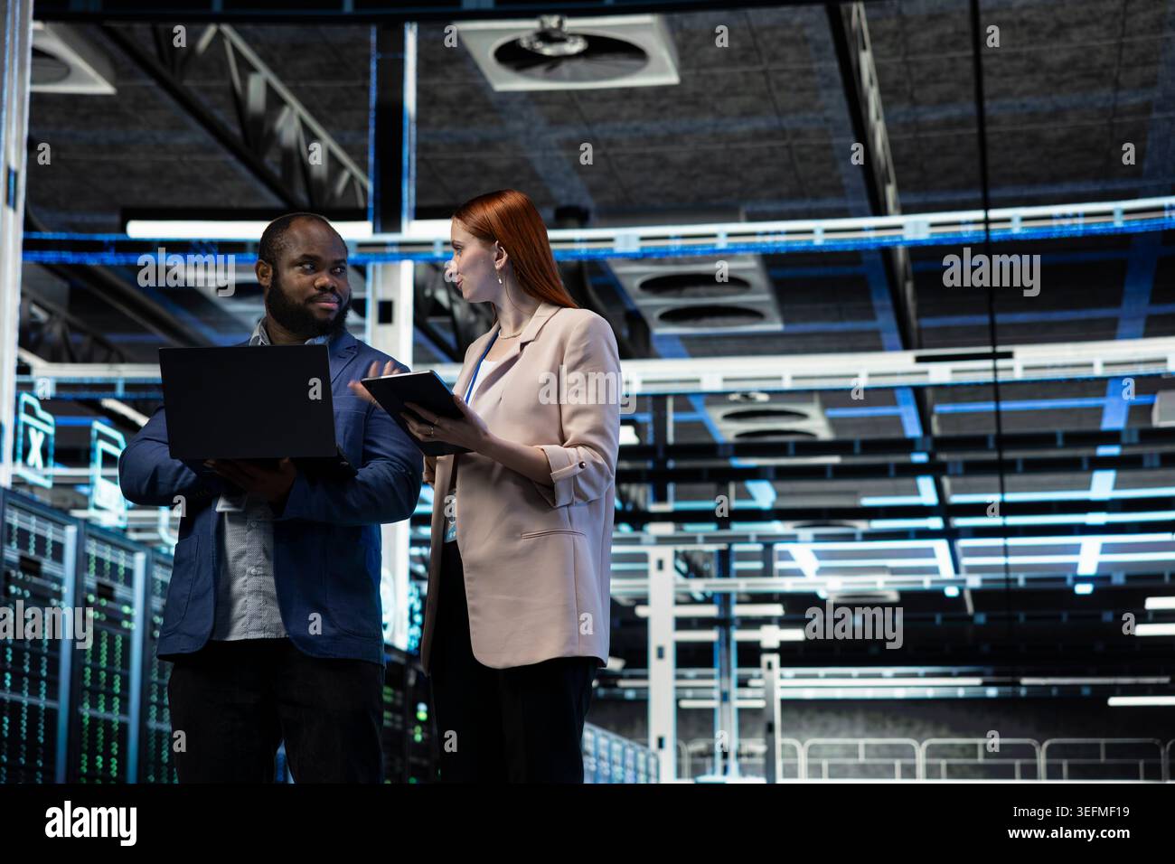Data center engineering team monitoring system performance, identifying bottlenecks. Server farm teamworking colleagues using devices to implement optimizations improving efficiency Stock Photo