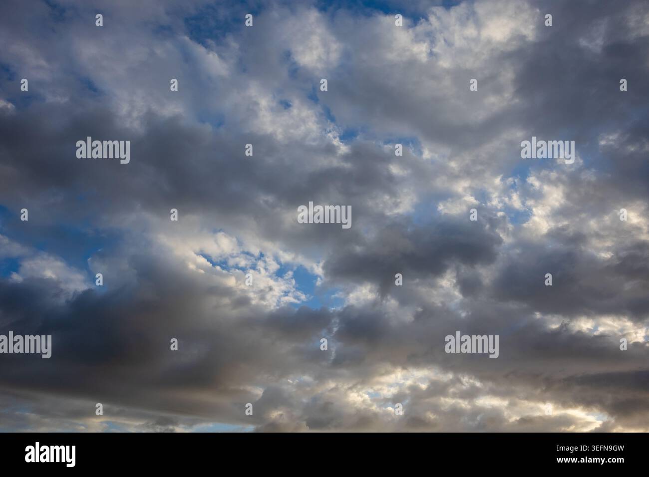 Mixed cloud formations with bright white cumulus and dark grey masses against vivid blue sky creating strong contrast Stock Photo