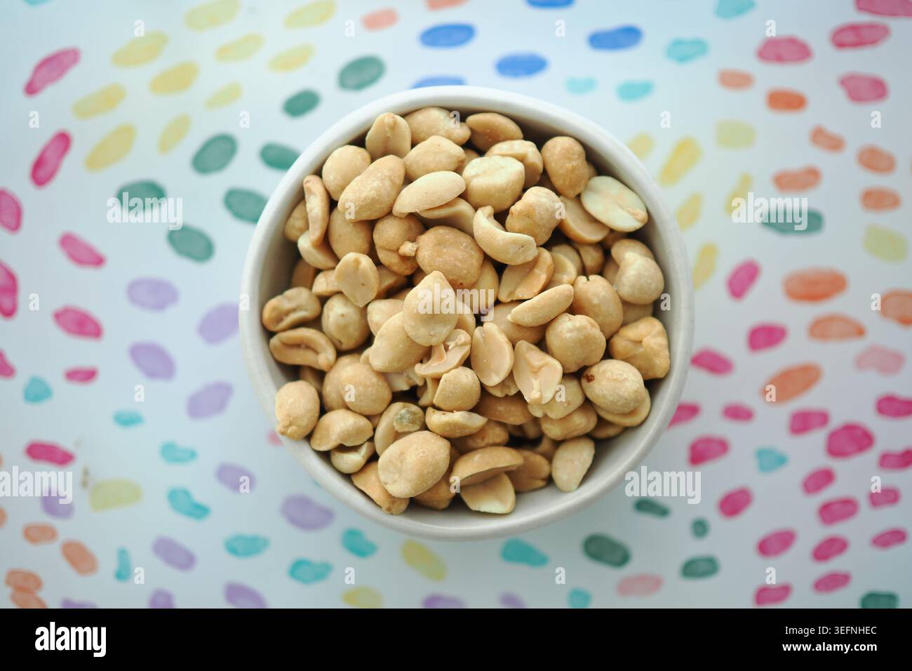 Snack bowl filled with roasted peanuts on colored background Stock Photo