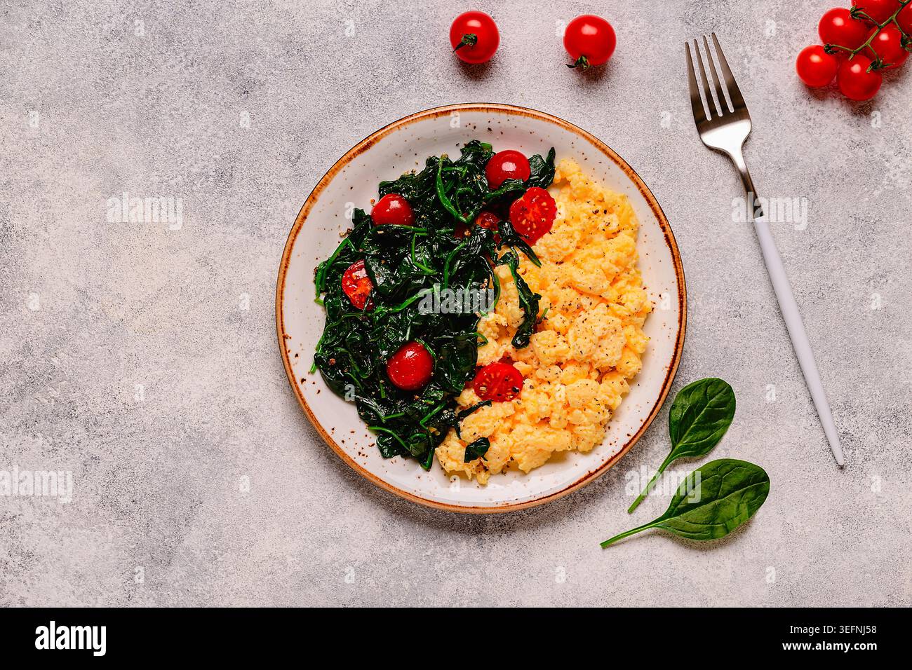 Cooked omelette and spinach with tomatoes on a light background, top view. Stock Photo