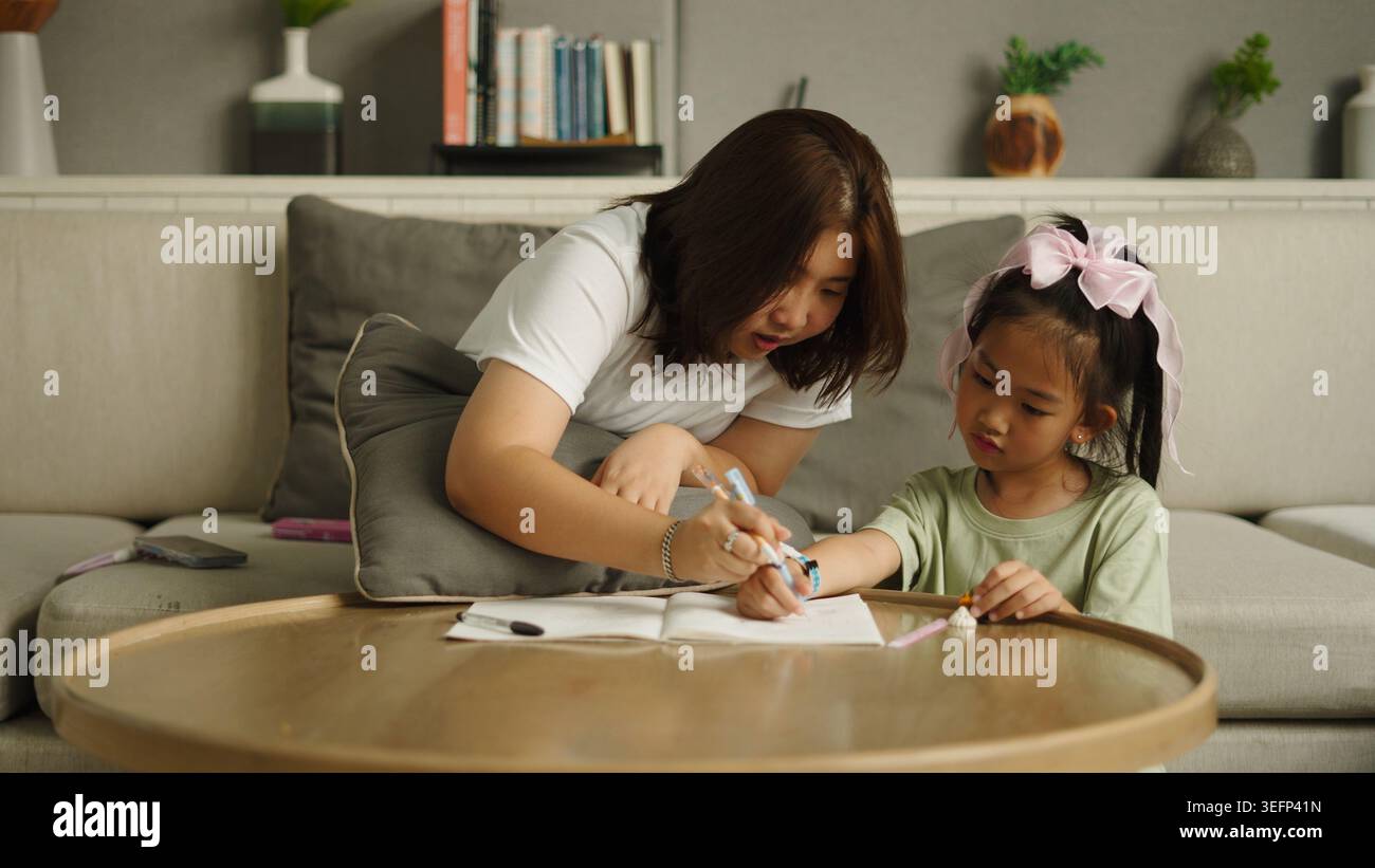 Mother helping child drawing in notebook, learning and bonding at home Stock Photo