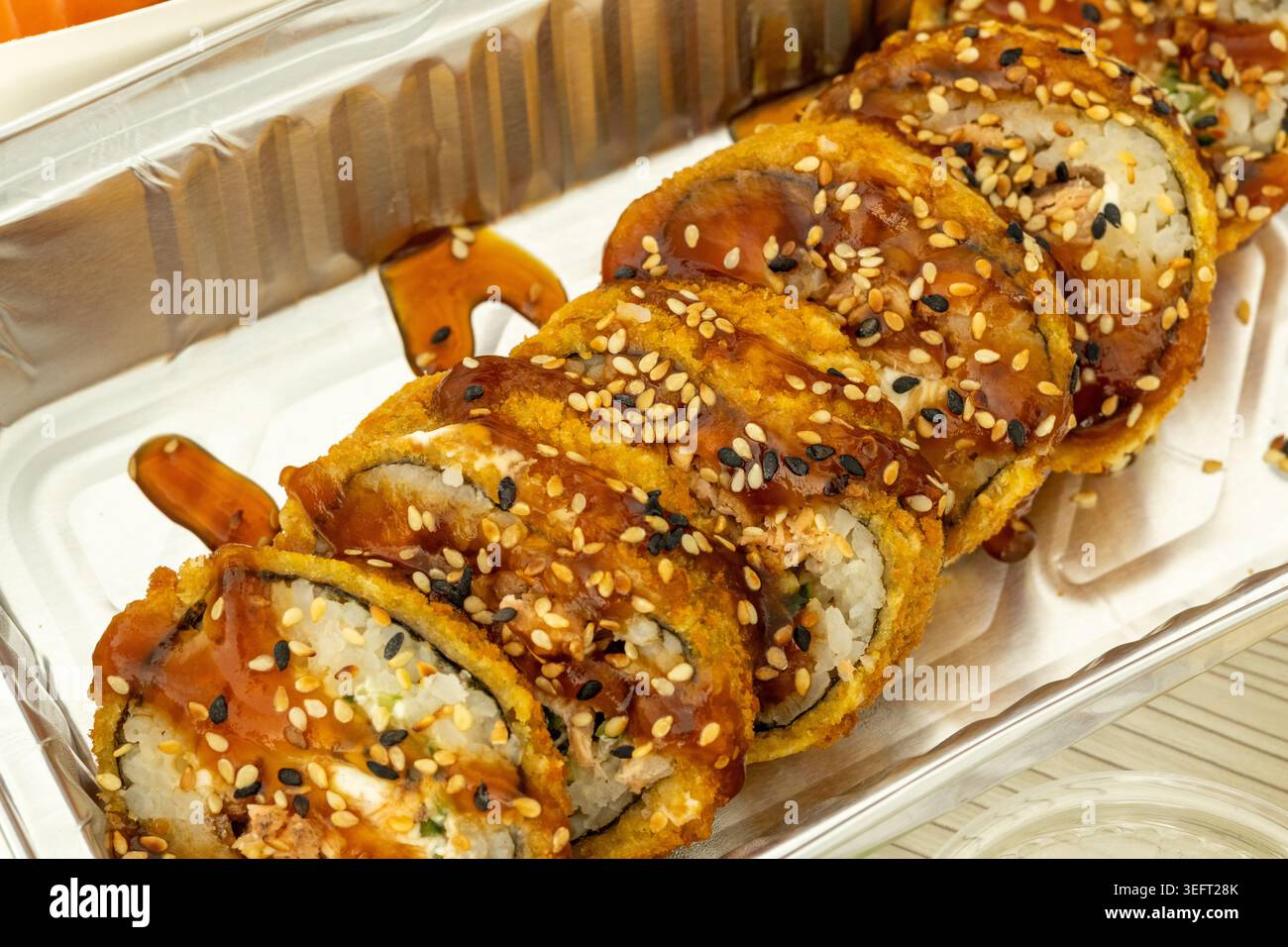 Crispy fried sushi rolls with sesame seeds and sweet soy sauce in a plastic takeout container Stock Photo
