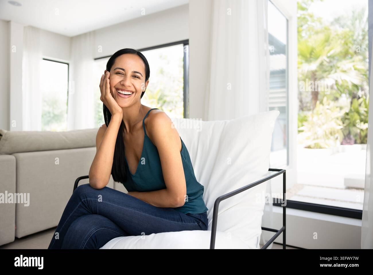 Cheerful woman sitting comfortably in sunlit living room Stock Photo