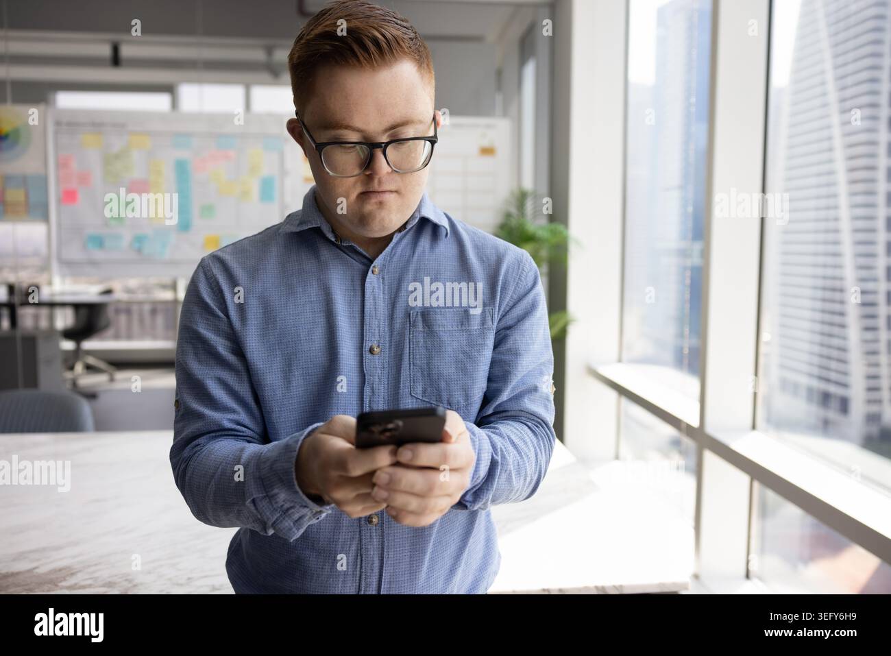 Serious man with Down syndrome using smartphone during work break Stock Photo