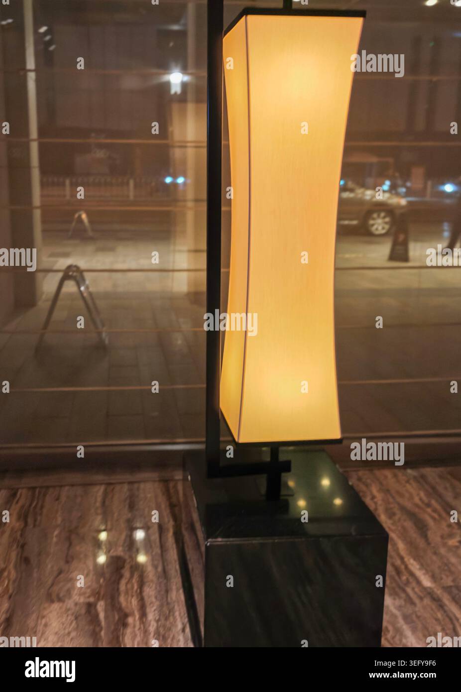 Modern floor lamp with a curved shade illuminated in a stylish interior setting, showcasing a sleek black base and warm light against a marble floor Stock Photo