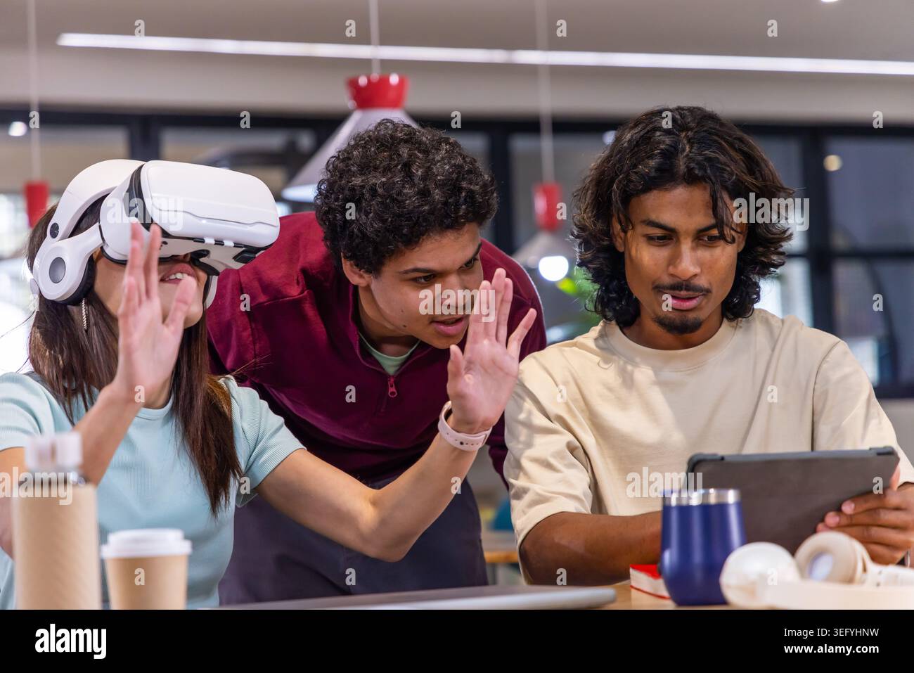 Diverse students collaborating at co-working table, interacting with white VR headset and tablet Stock Photo