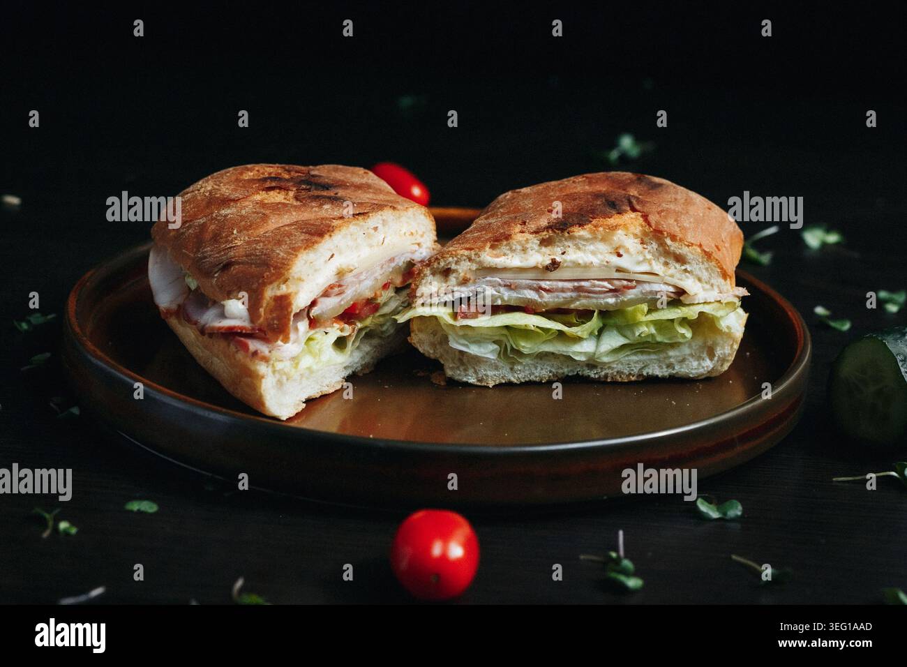 Delicious sandwich cut in half on wooden plate, surrounded by fresh ingredients Stock Photo