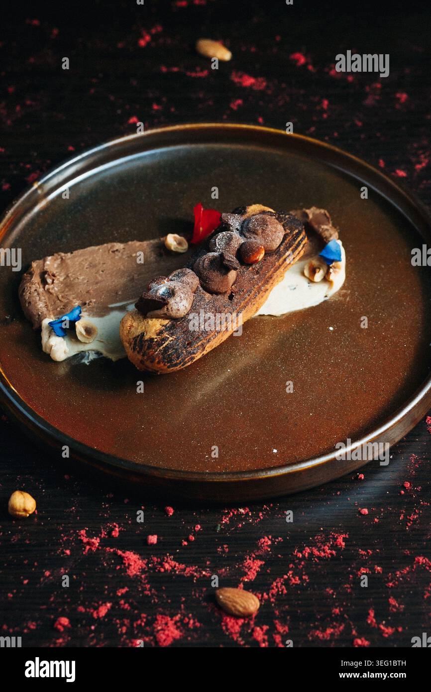 Chocolate eclair with toppings, served on a dark plate Stock Photo