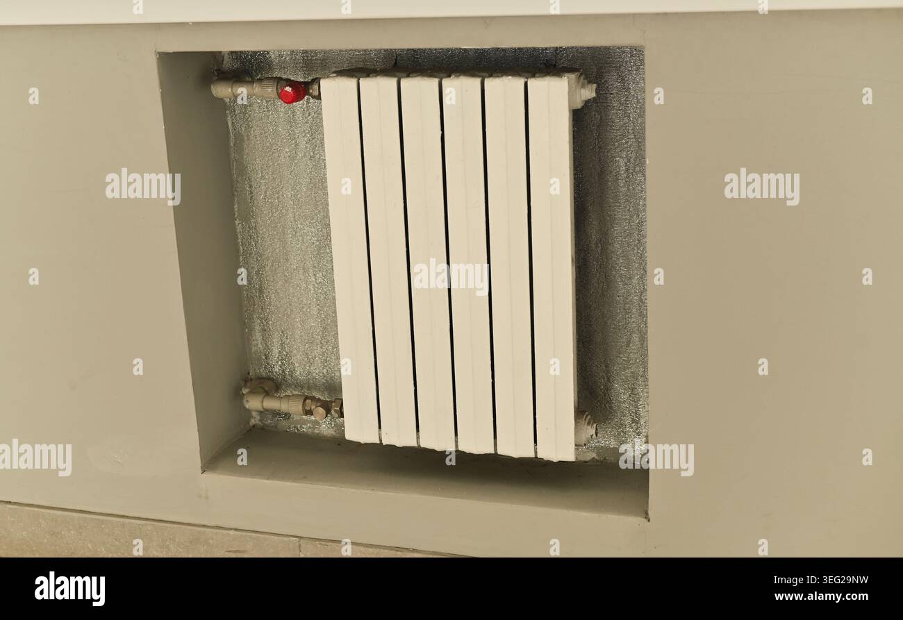 Wall-mounted radiator with white panels installed under window, indoor heating element providing warmth in modern interior, functional and practical d Stock Photo