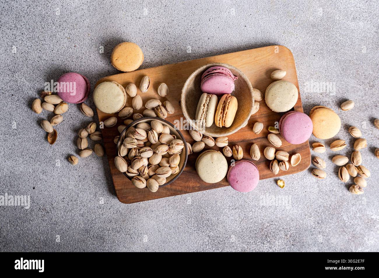 Colorful macarons in various flavors, including pistachio, are artfully placed on a wooden board with scattered pistachios, creating a delightful and Stock Photo
