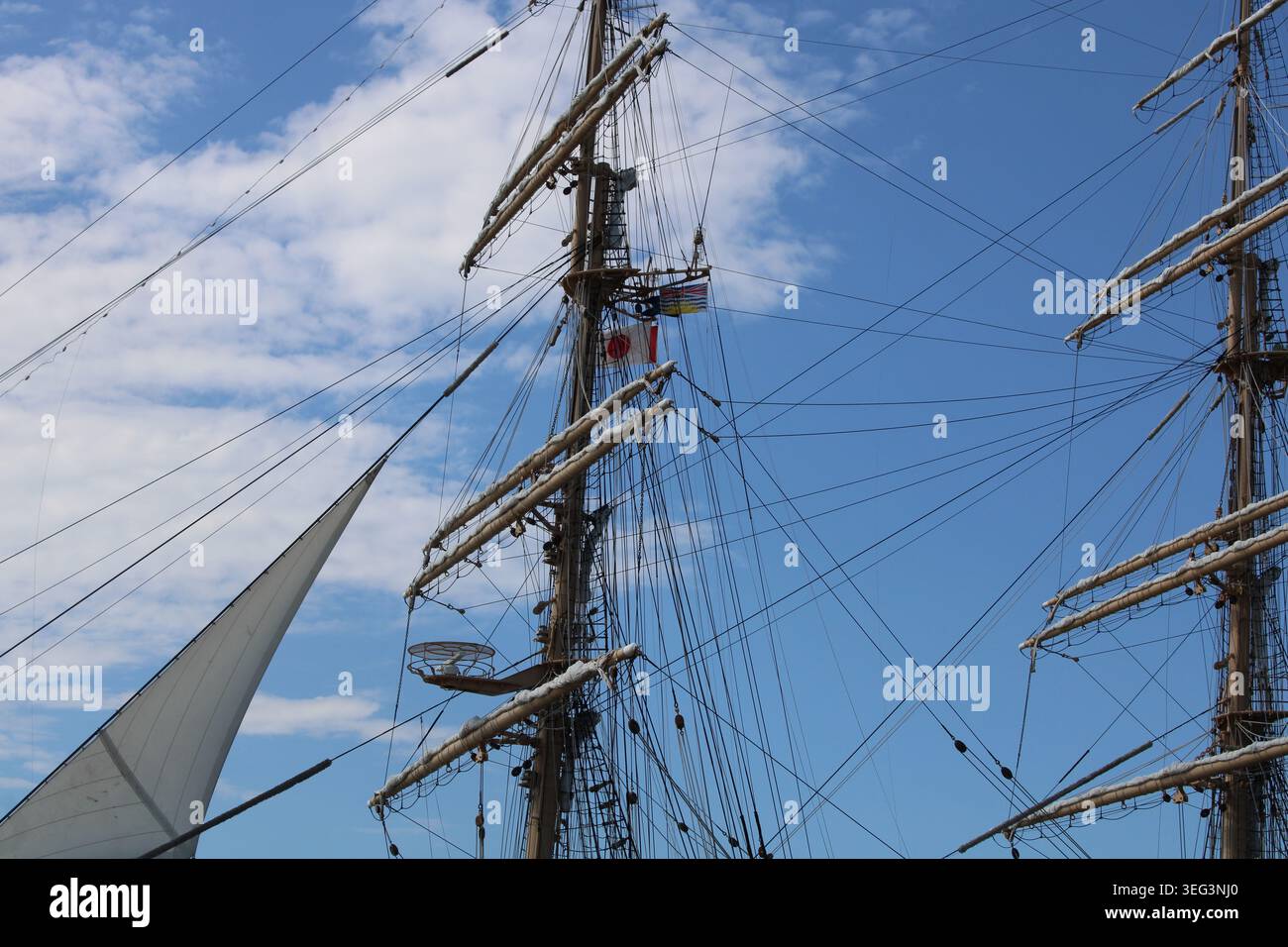 Tall ship masts with rigging rise into a bright blue sky with flags of ...