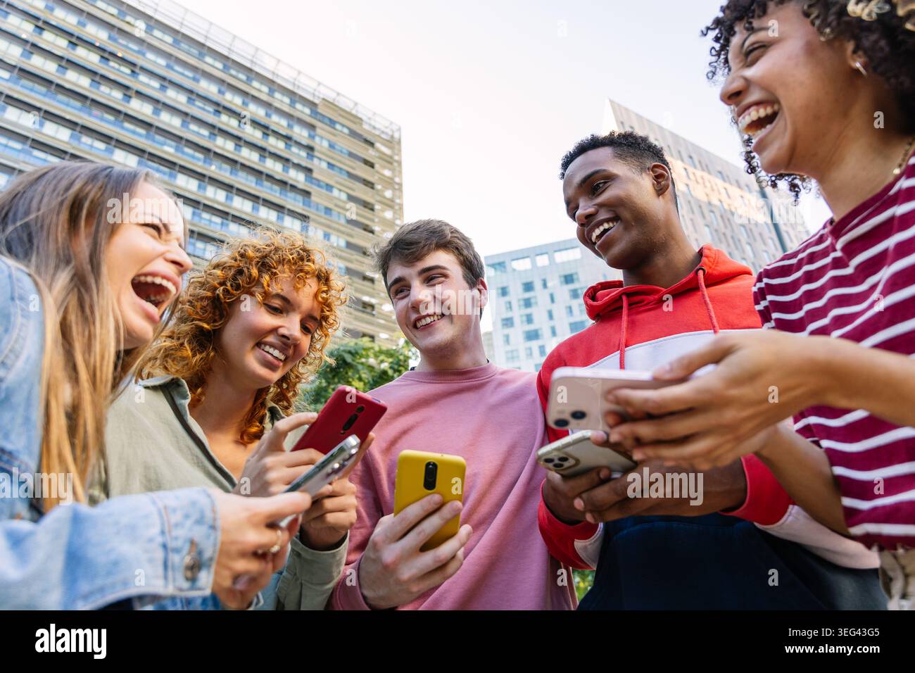 Diverse gen z friends laughing displaying smartphones outdoors Stock Photo