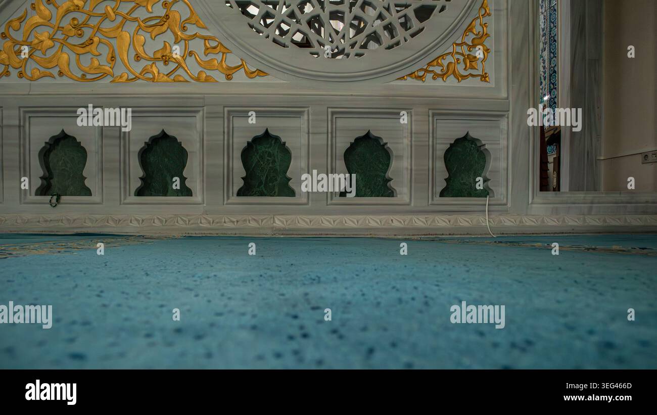 ISTANBUL, Türkiye - April 30, 2026.Green marble niches are set into a white stone wall over a soft turquoise prayer carpet. Stock Photo