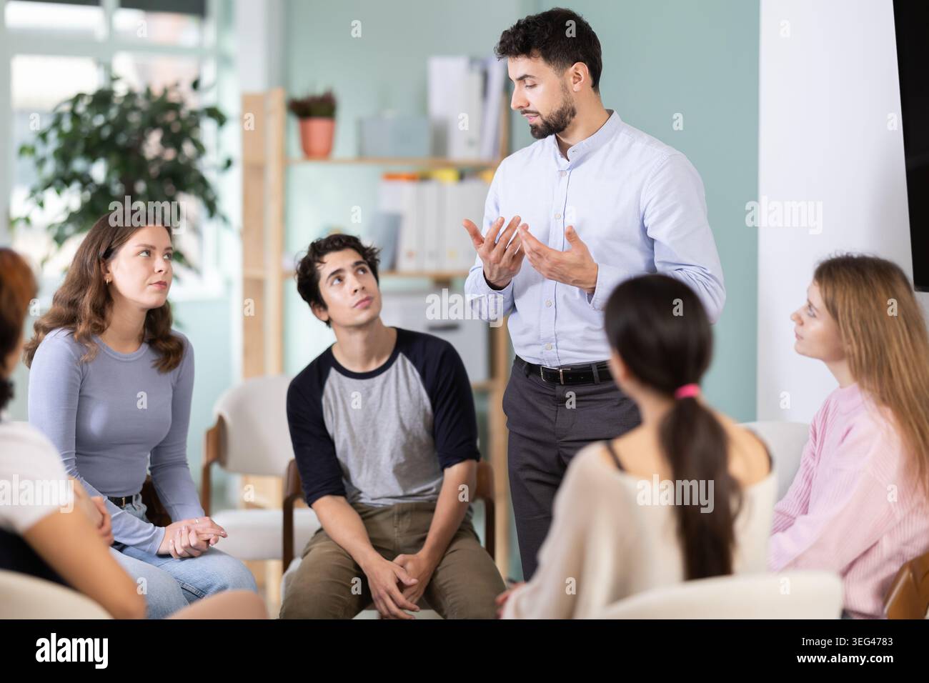 Male teacher talking to interested students sitting in a circle Stock Photo