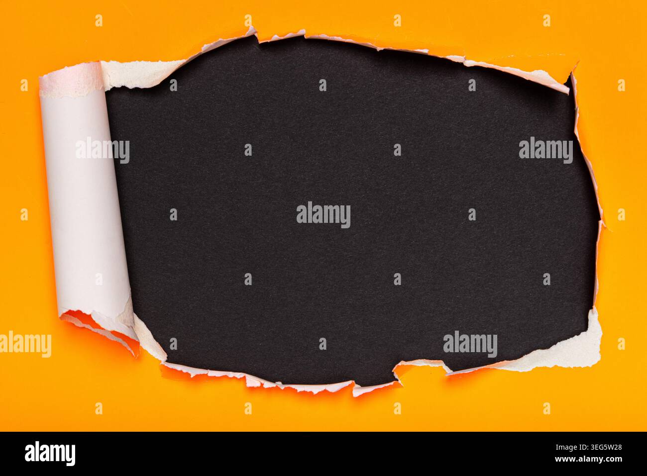 A vibrant orange paper is torn open, revealing a textured black surface underneath. Stock Photo