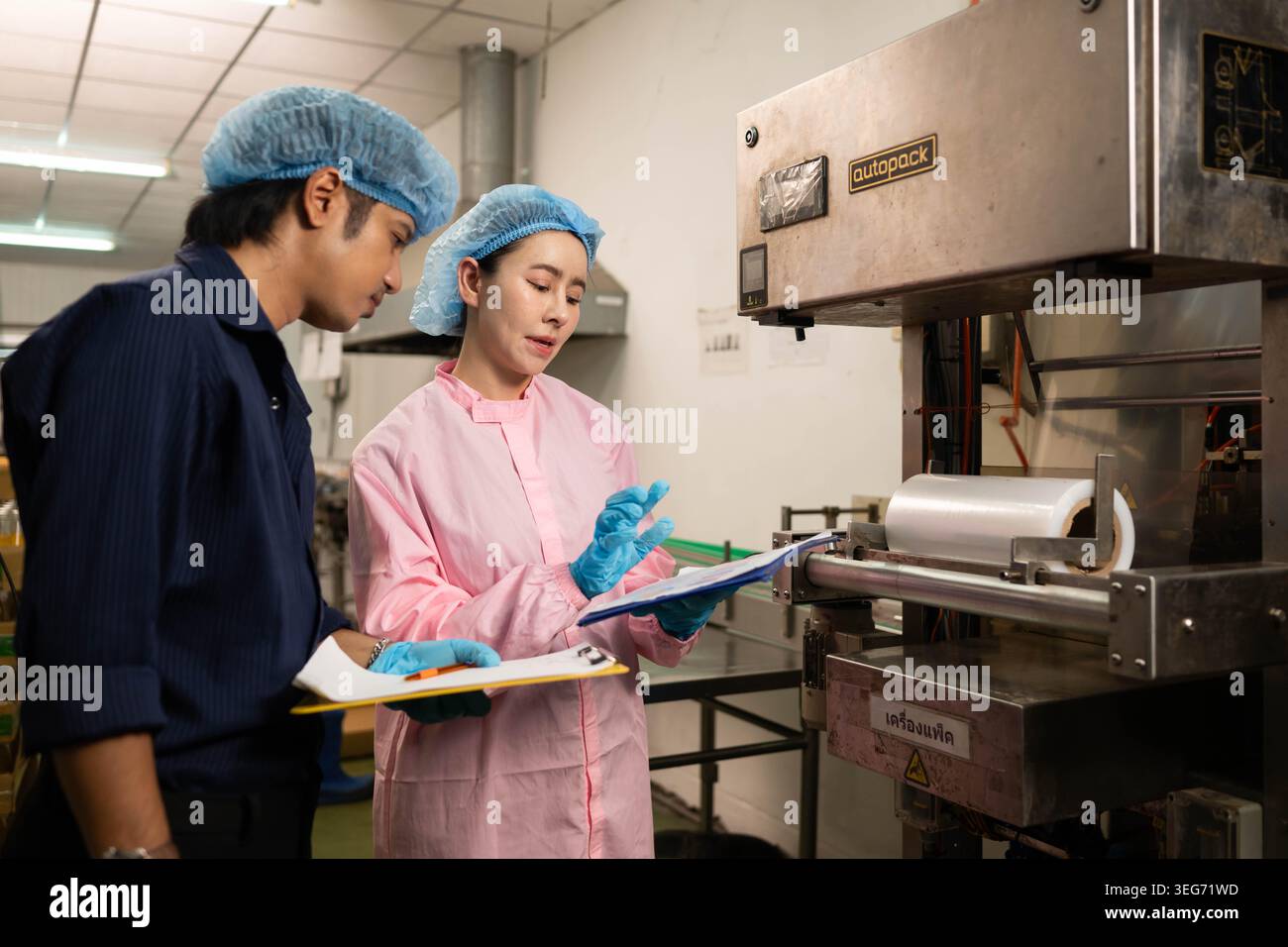 Two workers inspecting packaging machine and recording data in beverage production process Stock Photo