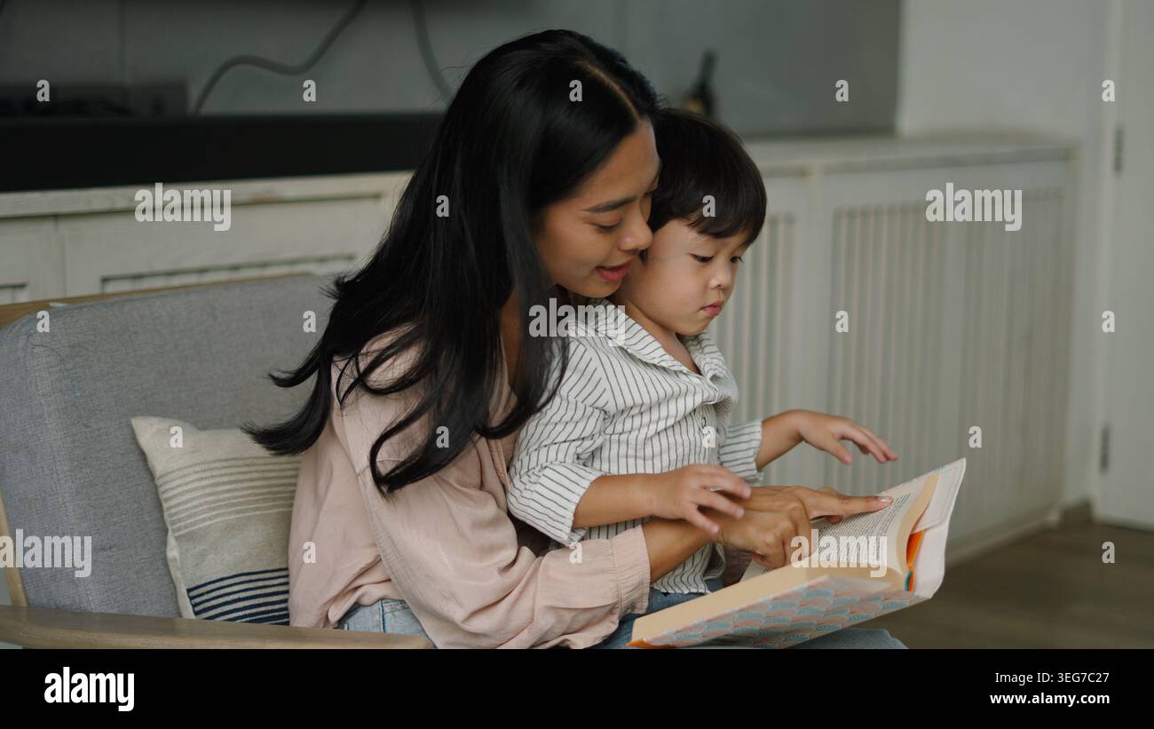 Woman and boy sitting on a couch, pointing at an open book, engaging in ...
