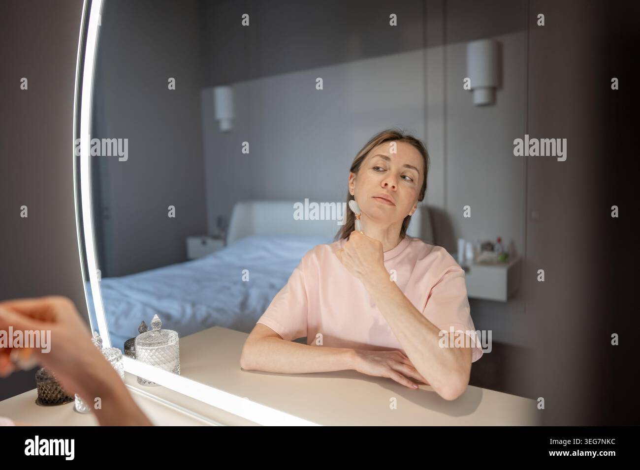 Middle-aged woman sits in front of mirror applying skincare product to ...