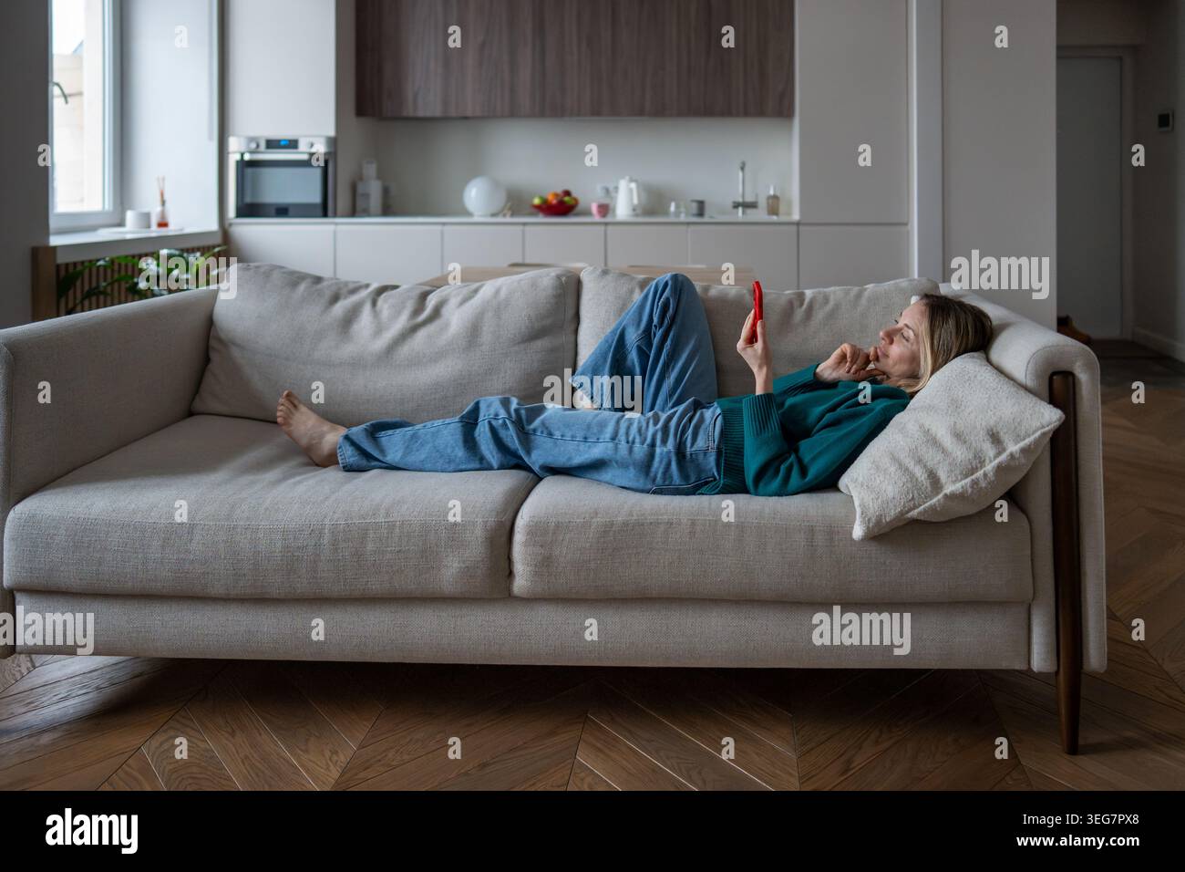Contented middle aged woman using phone lounging on sofa online shopping with interest from home. Stock Photo
