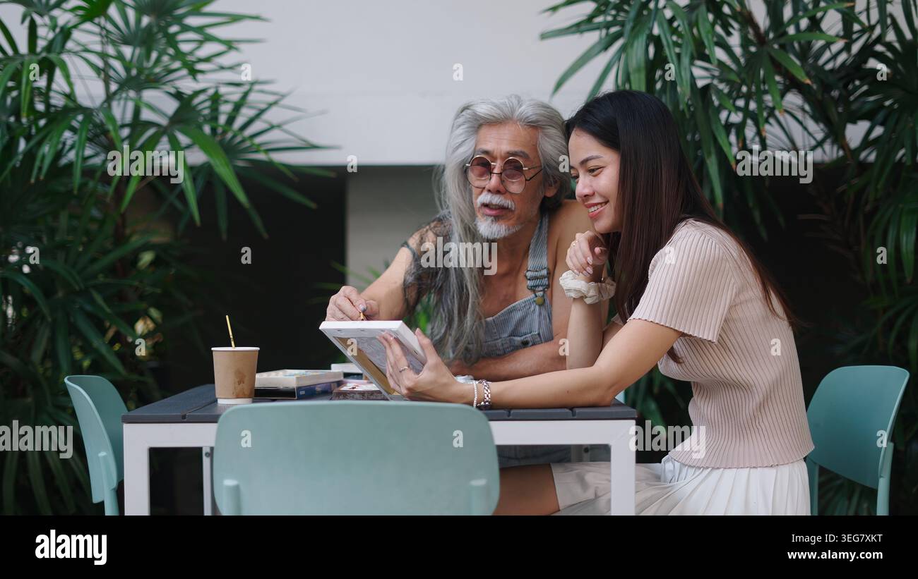 Senior man and young woman discussing art, sharing creative ideas at outdoor cafe Stock Photo