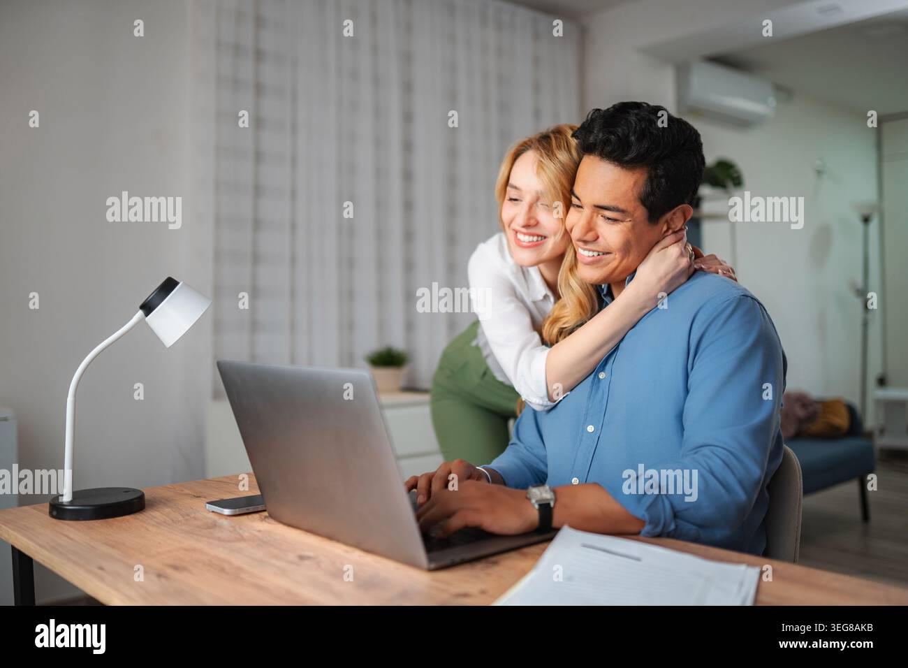 Happy couple working from home using laptop embracing Stock Photo