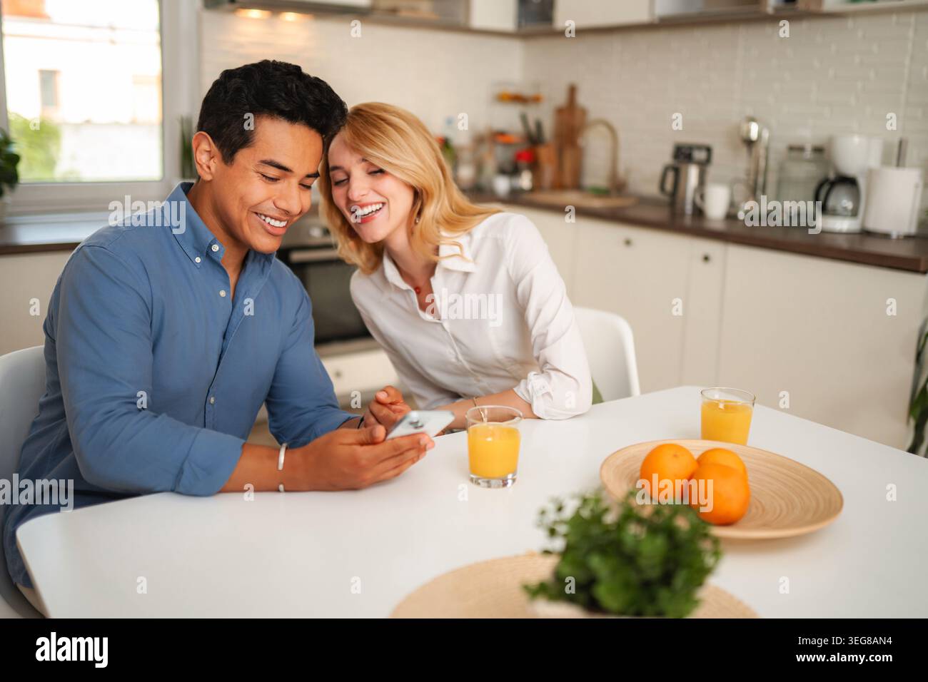 Happy couple laughing watching content on smartphone in kitchen Stock Photo