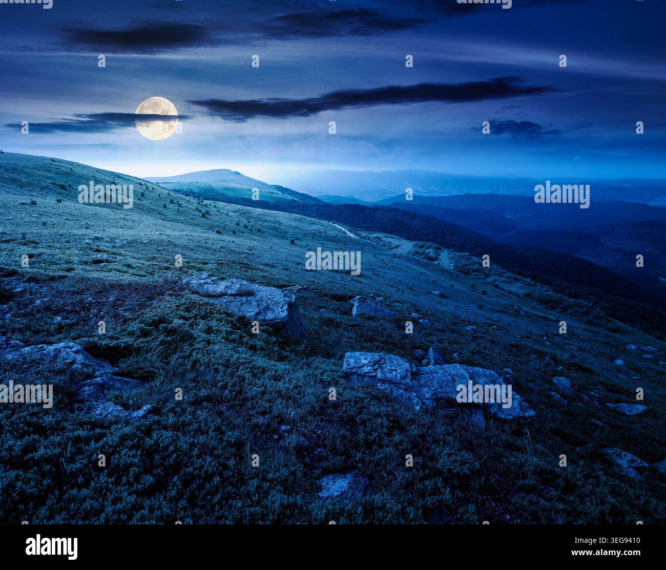 mountain summer landscape at night. full moon over meadow with giant stones among the grass on the hillside. mysterious view near the peak of mountain Stock Photo