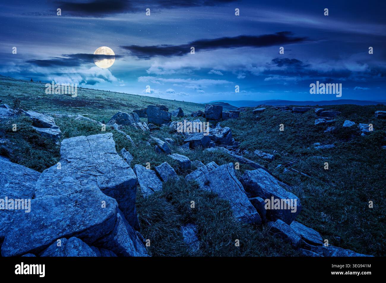 mountainous landscape during summertime at night. full moon over boulders and rock formations surrounded grassy hills. picture of an untouched highlan Stock Photo