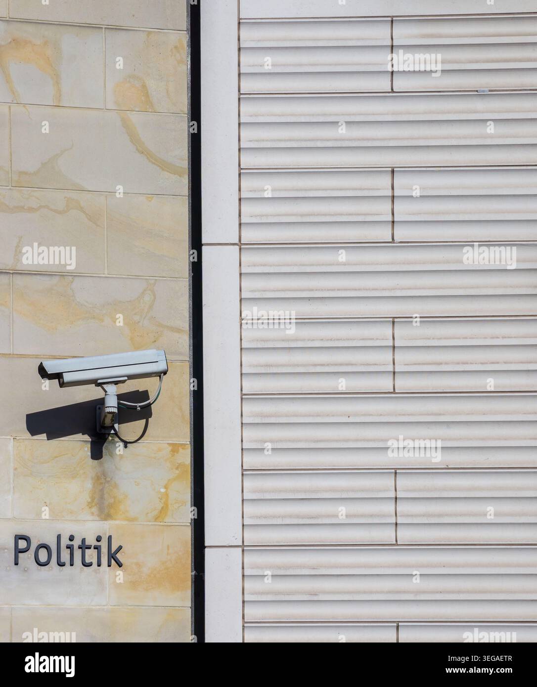 Close-up of a surveillance camera mounted on a building facade beside the word “Politik”, creating a visual concept of security and monitoring. Stock Photo