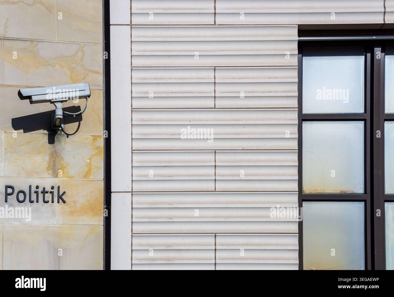 Close-up of a surveillance camera mounted on a building facade beside the word “Politik”, creating a visual concept of security and monitoring. Stock Photo