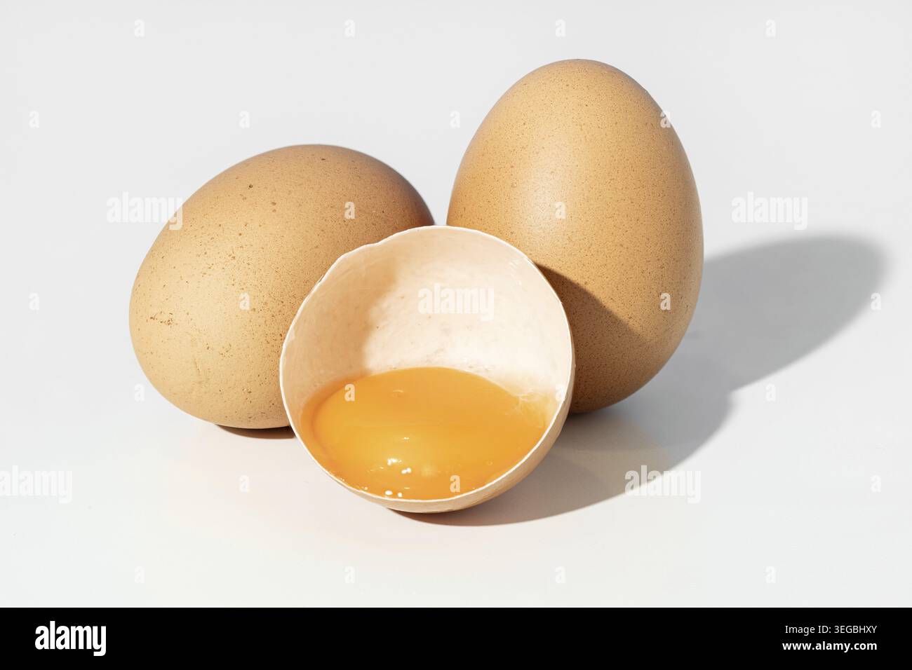Studio shot of Two whole brown eggs and a broken eggshell containing an egg yolk isolated on white background Stock Photo