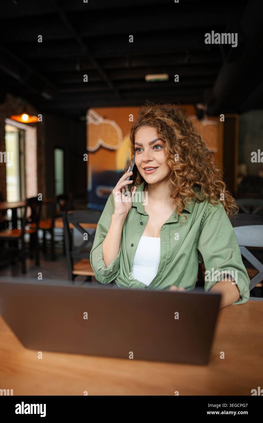 Freelancer working remotely from cafe, talking on phone and using laptop Stock Photo