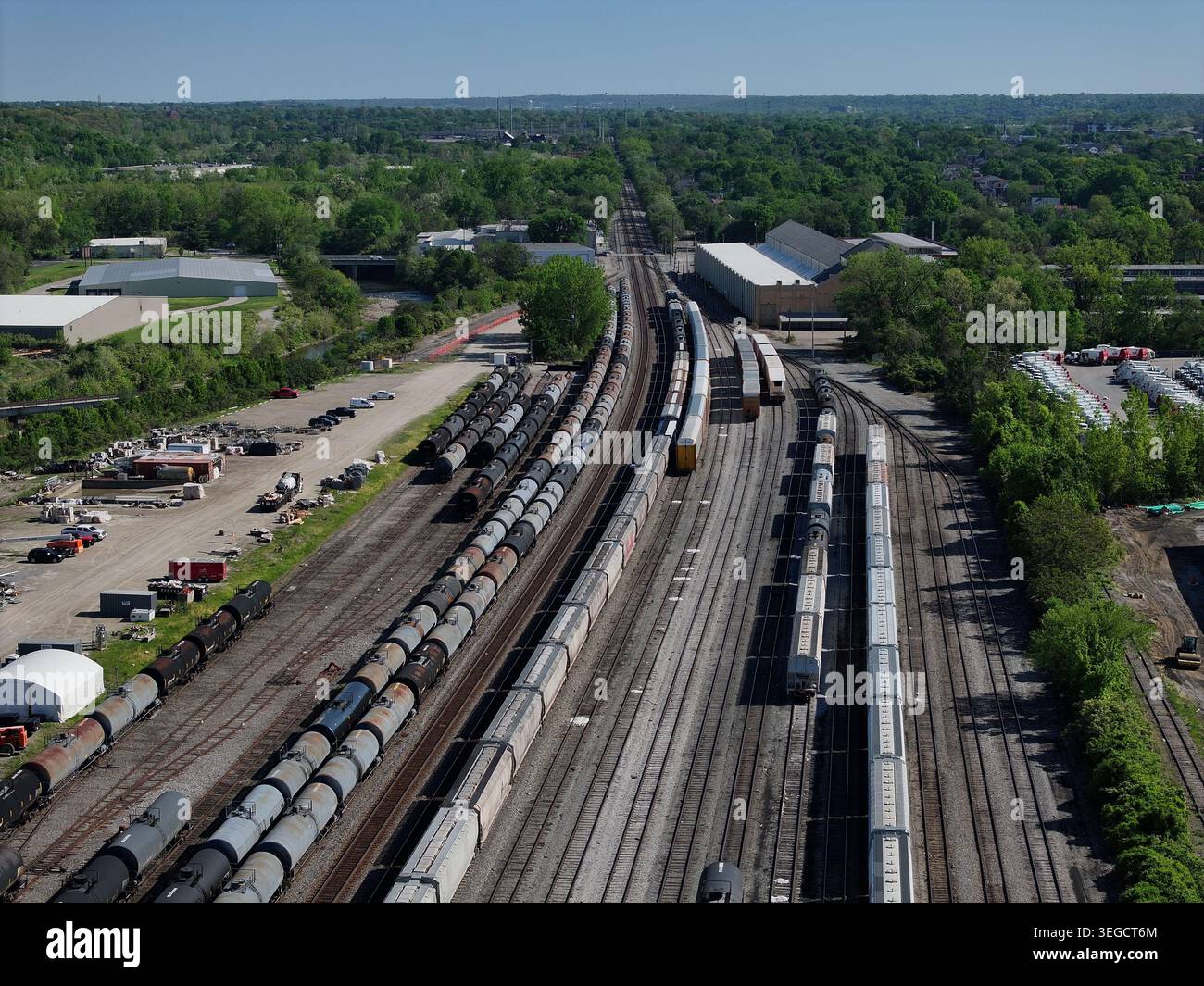 Aerial view of freight trains parked on multiple tracks in a railway yard surrounded by lush green trees and industrial buildings Cincinnati, OH, Unit Stock Photo