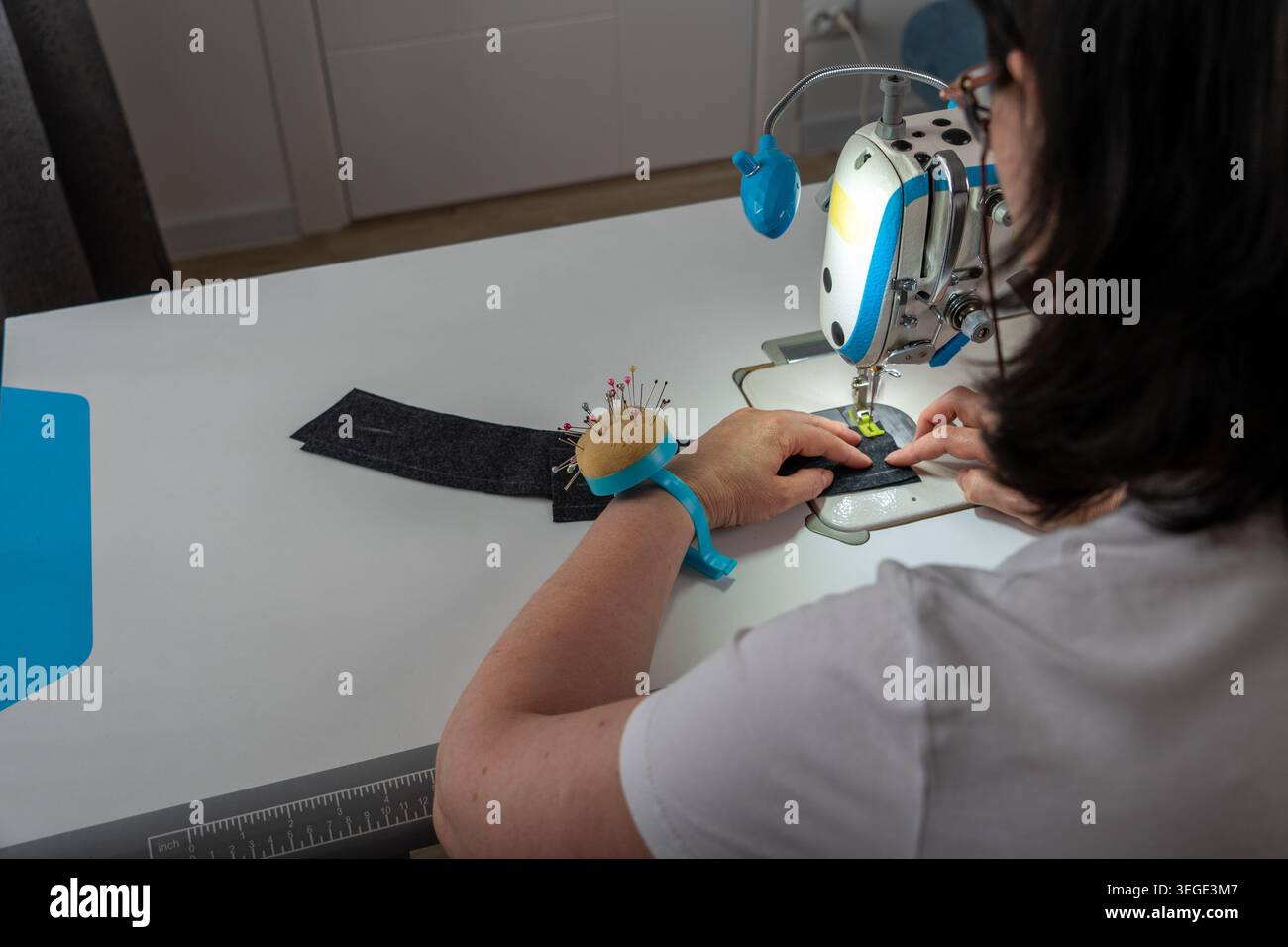 Female seamstress sewing clothes and working with textile materials in creative workshop. Back view of dressmaker during tailoring process with sewing Stock Photo