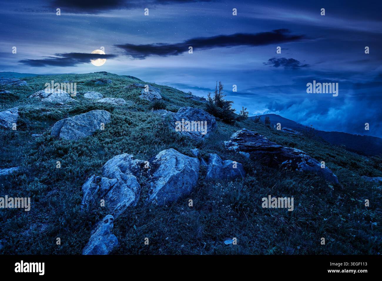 green landscape of mountain in summer at night. mysterious view of rock among grass on the hillside. full moon over travel background under a dark sky Stock Photo