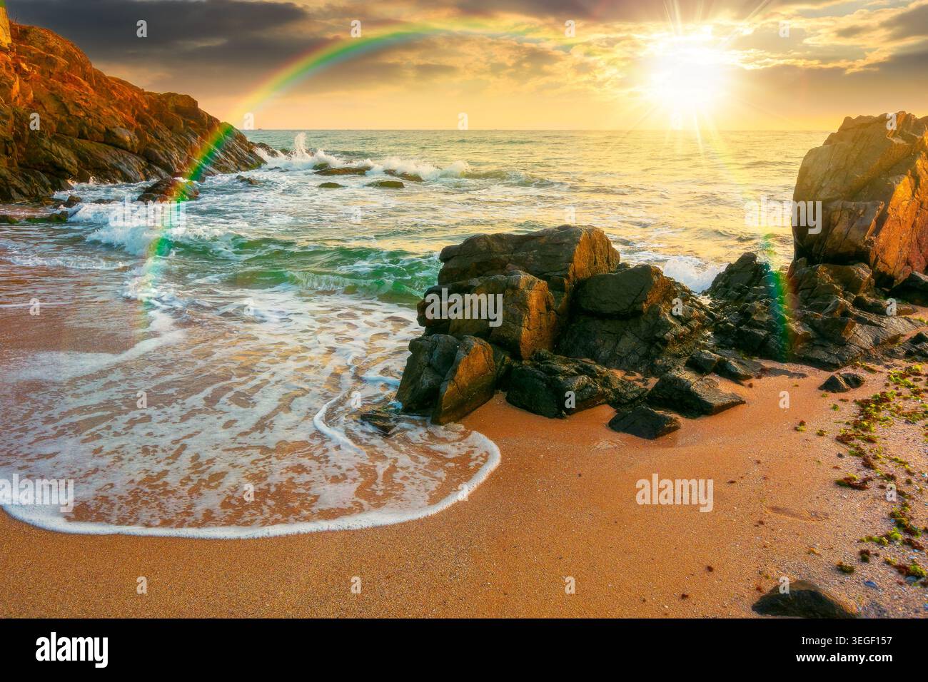 sunset over huge stones on the sandy beach. wonderful holiday season background at the sea. clouds on the blue sky above horizon. view of waves washin Stock Photo