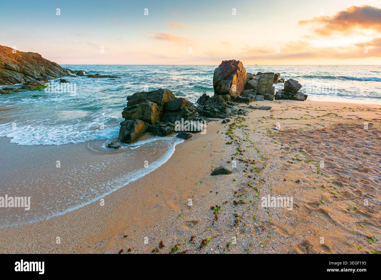 huge stones on the sandy beach at sunrise. wonderful holiday season background at the sea. clouds on the blue sky above horizon. view of waves washing Stock Photo