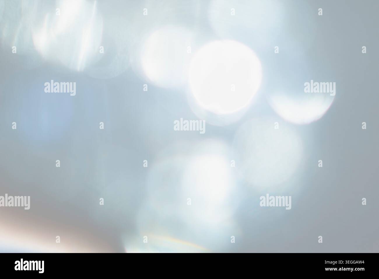Defocused bright white bokeh lights on pale blue background Stock Photo