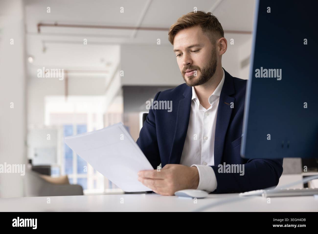 Focused young businessman reading and analyzing documents with serious expression Stock Photo