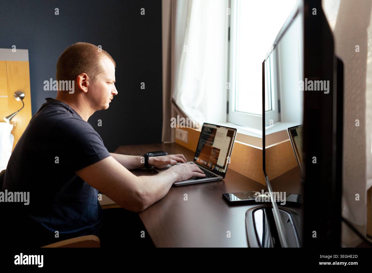 Man typing on a laptop, coding, working remotely from a hotel desk Stock Photo