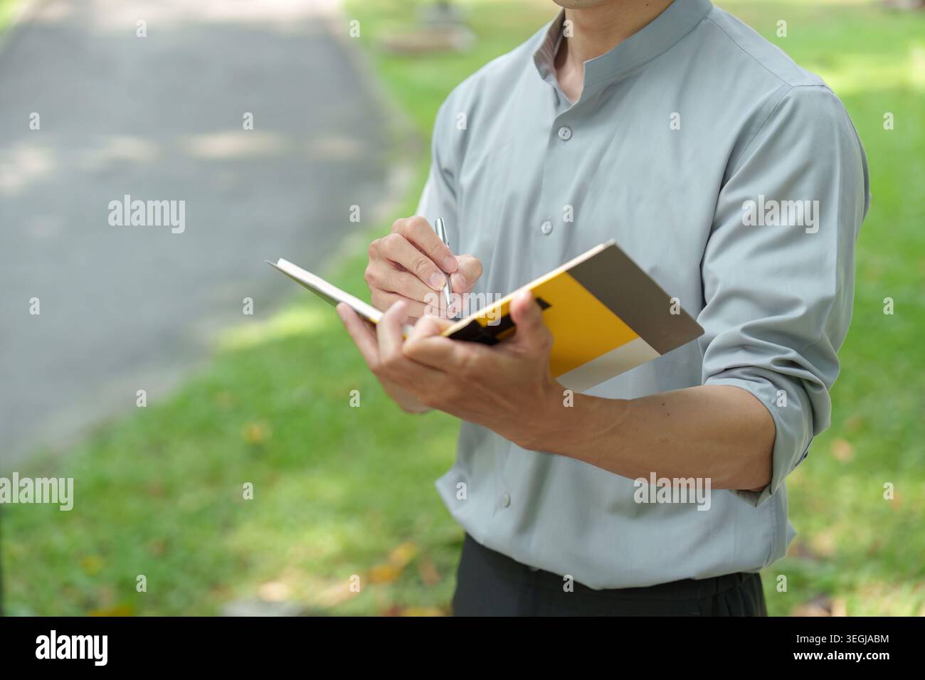 Asian man writing notes in notebook outdoors in park Stock Photo