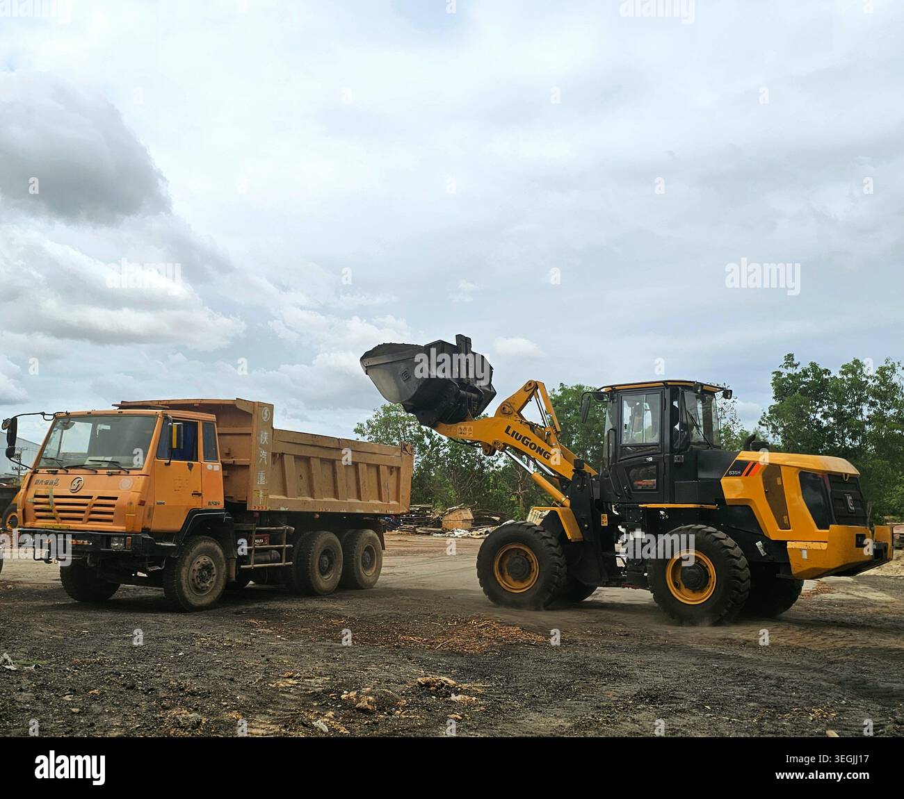 Wheel loader positioned beside a dump truck at an industrial yard under cloudy skies, showcasing heavy equipment operations. - Smartphone Captured Stock Image