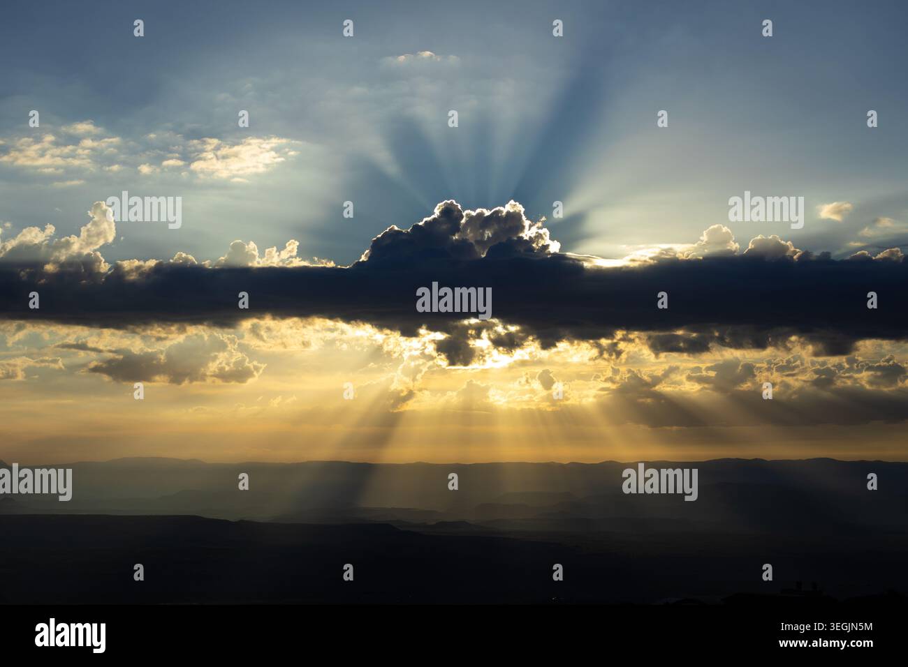 Spectacular sun rays streaming through dramatic storm clouds over a vast desert valley landscape at sunset. Golden light beams illuminate layered moun Stock Photo