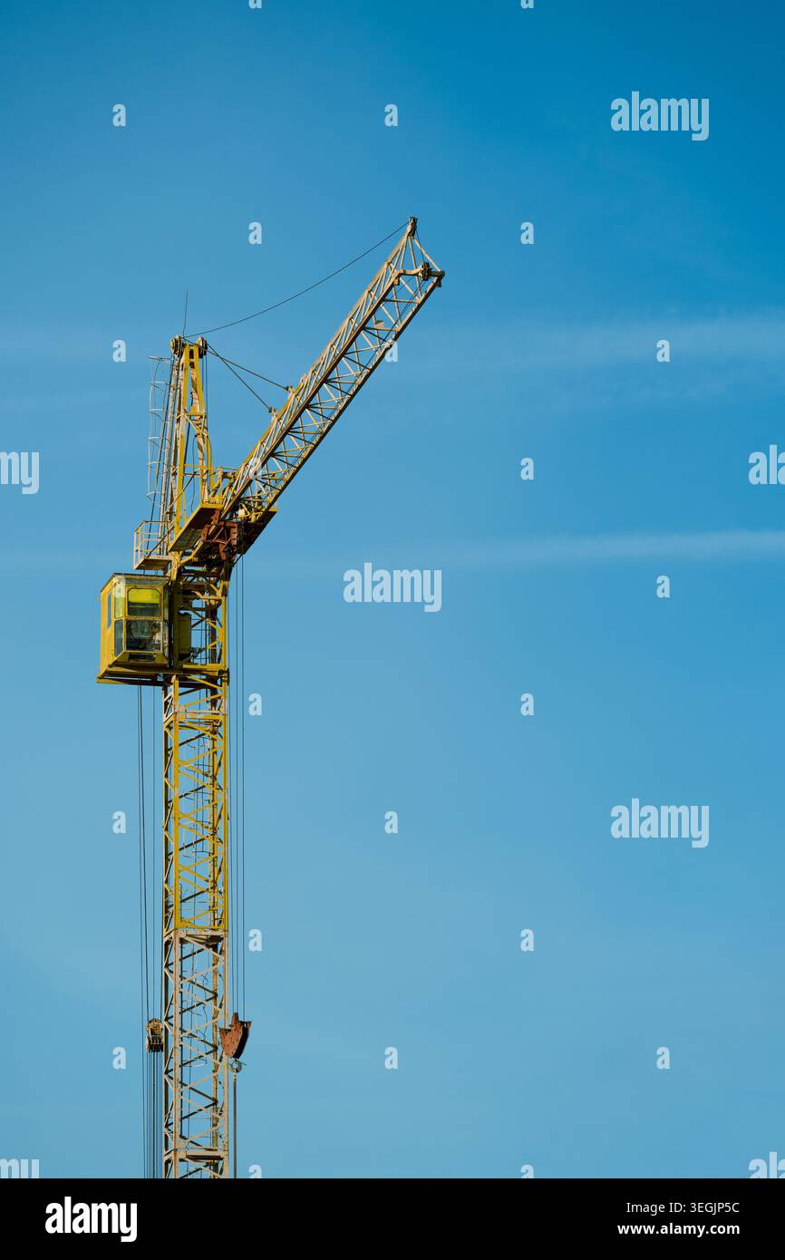 Yellow construction tower crane against clear blue sky, low angle view. Stock Photo