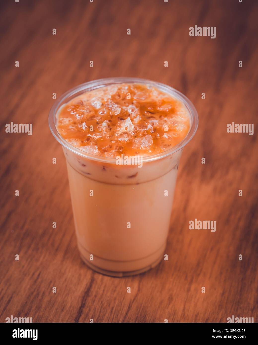 Iced milk tea with crushed ice in a clear plastic cup on a wooden table Stock Photo